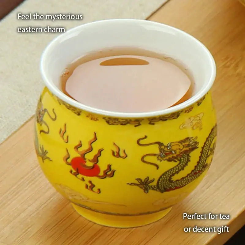 A vibrant yellow ceramic tea cup with gold and red dragon motifs and white interior from decorbites dragon teapot tea set