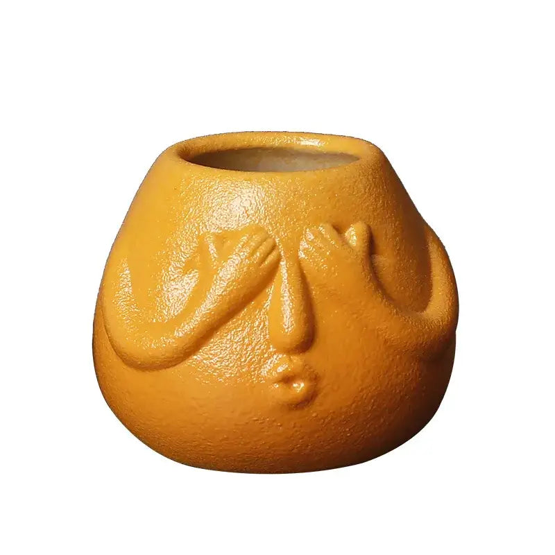 A matte orange ceramic abstract human face planter with hands covering eyes for decorbites ceramic abstract decor