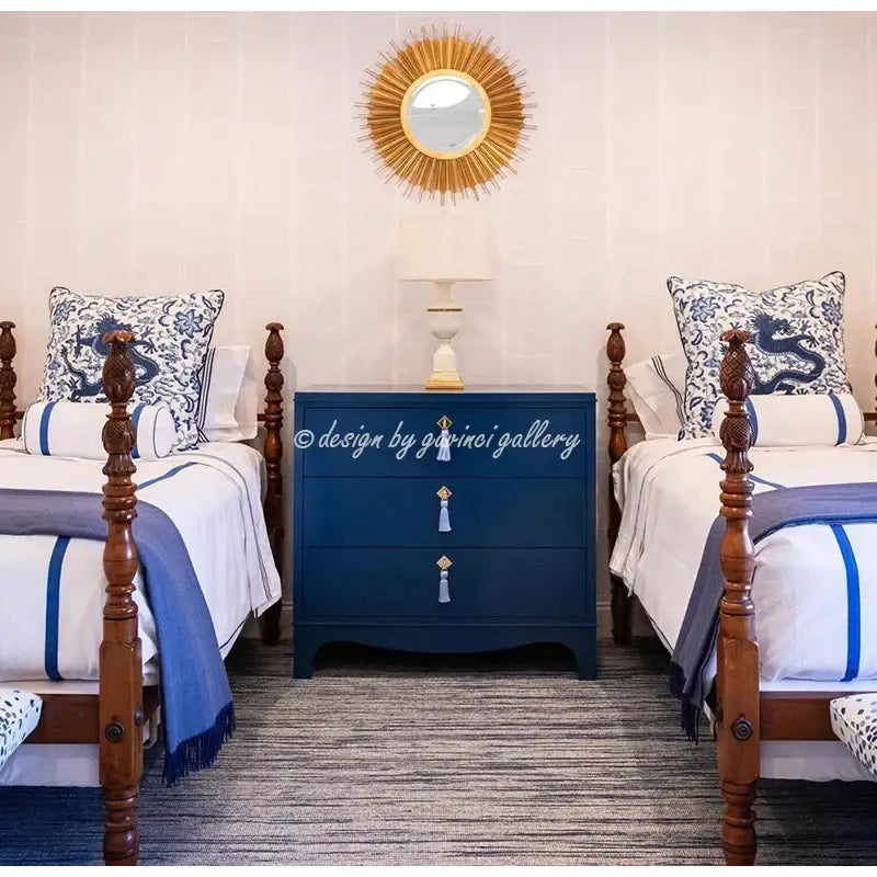 Navy blue three-drawer dresser with gold tassel pulls and a sunburst mirror above featuring a blue and white crane throw pillow case
