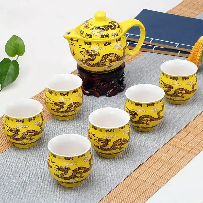Vibrant yellow double ceramic teaware set with intricate brown dragon designs and matching teapot on dark wooden stand