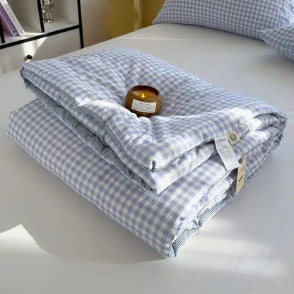 A neatly folded blue and white cotton summer quilt with gingham pattern and striped inner lining for bedroom use