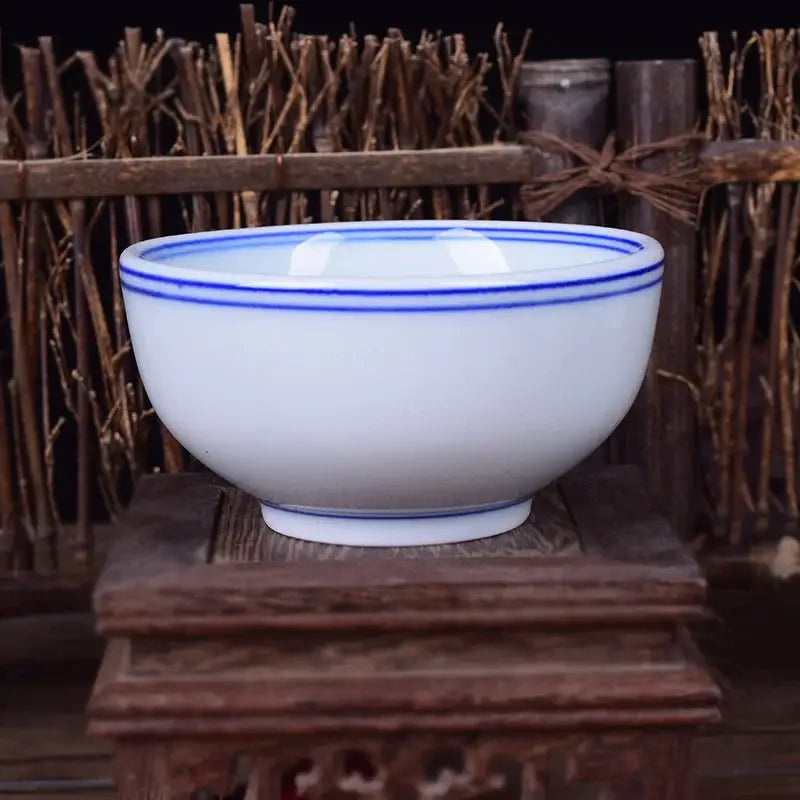 A white porcelain rice bowl with two thin blue bands on the rim resting on an ornate wooden stand