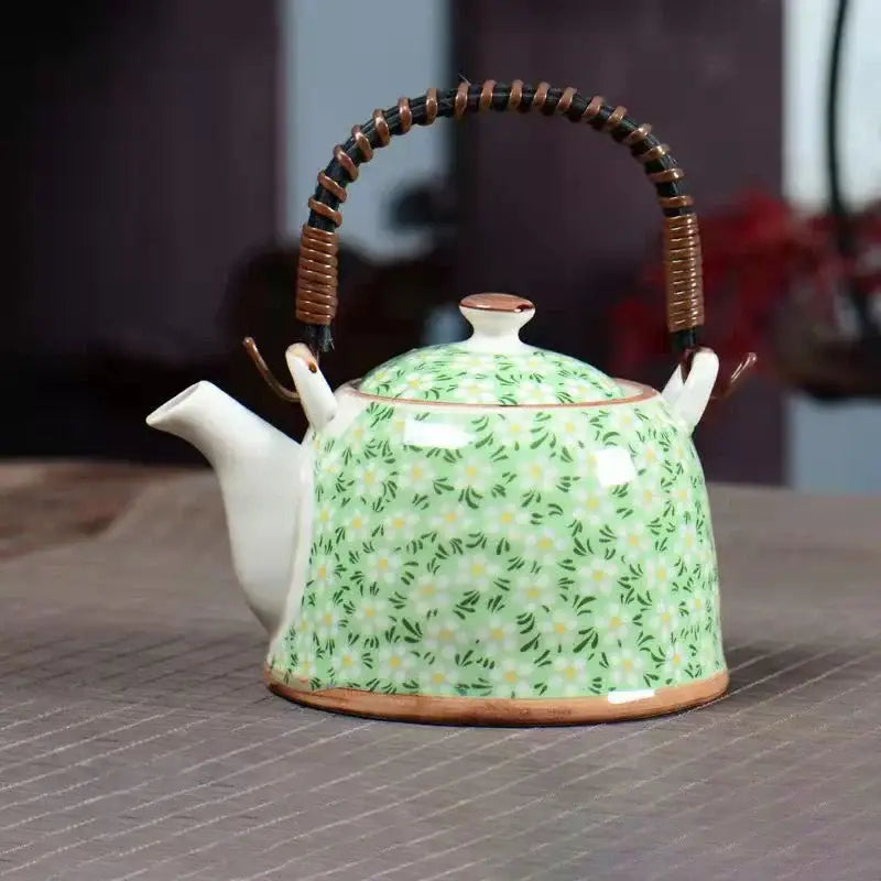 A light green ceramic teapot with yellow and green floral patterns, white porcelain spout and lid, and woven bamboo handle for dining room decorbites blue set