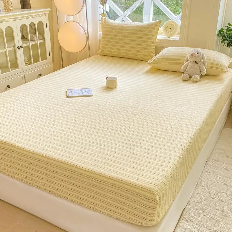 Cream-colored striped mattress pad with soft textured fabric complementing blue and white striped cotton fitted sheet set