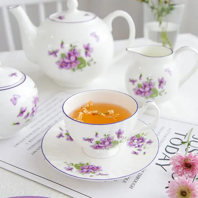 White porcelain teacup with purple violet floral design and blue rim filled with golden tea from blue dream tea set