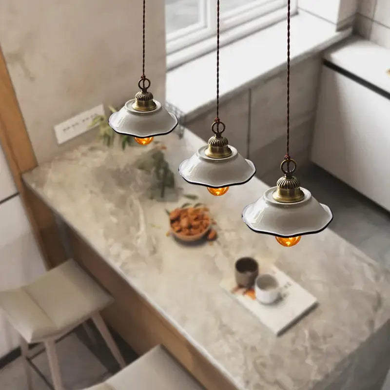 Three vintage-style decorbites ceramic led pendant lamps with white ceramic shades and brass accents above marble countertop