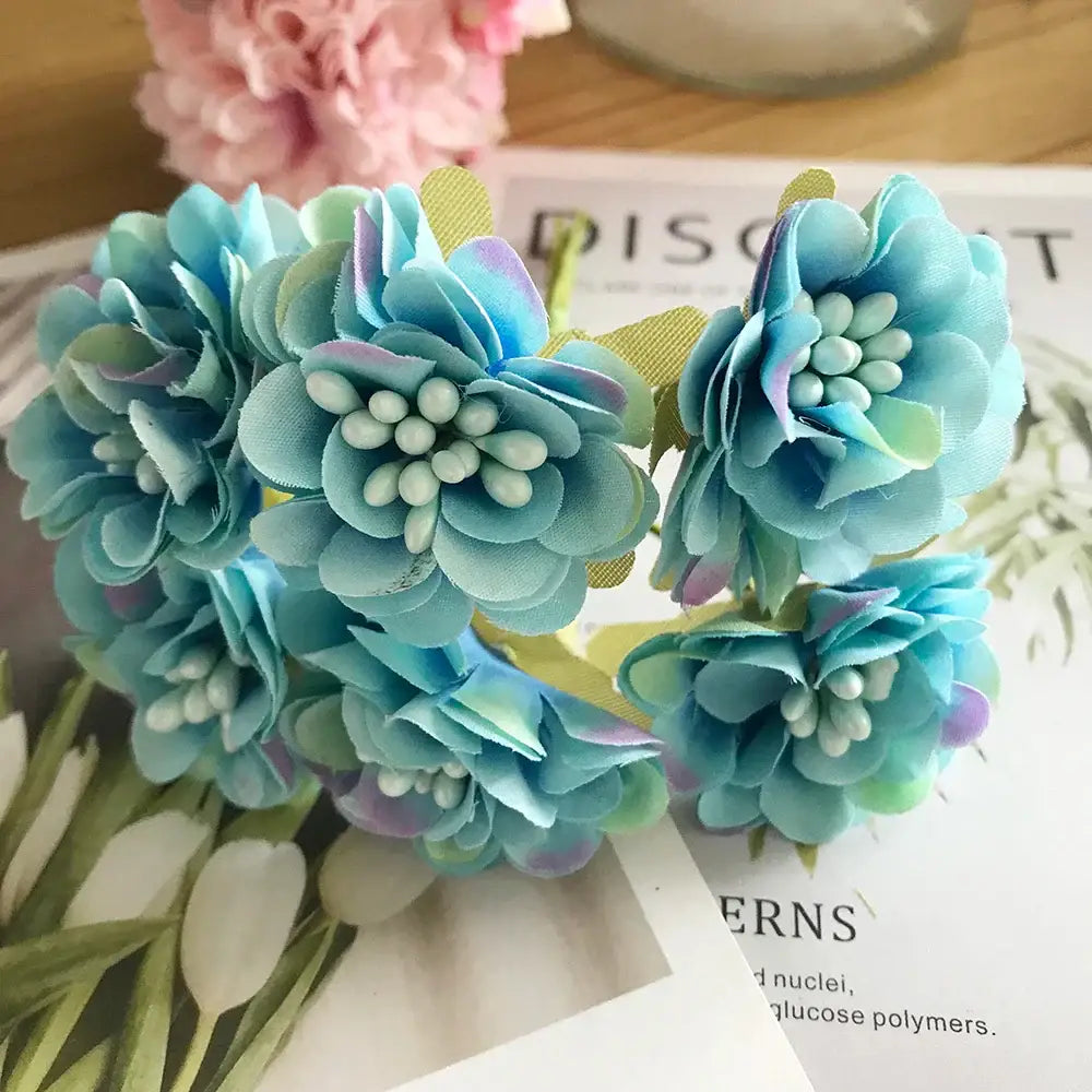 A cluster of decorbites blue flower cherry artificial fabric flowers in blue and green with white bead stamen centers for decor