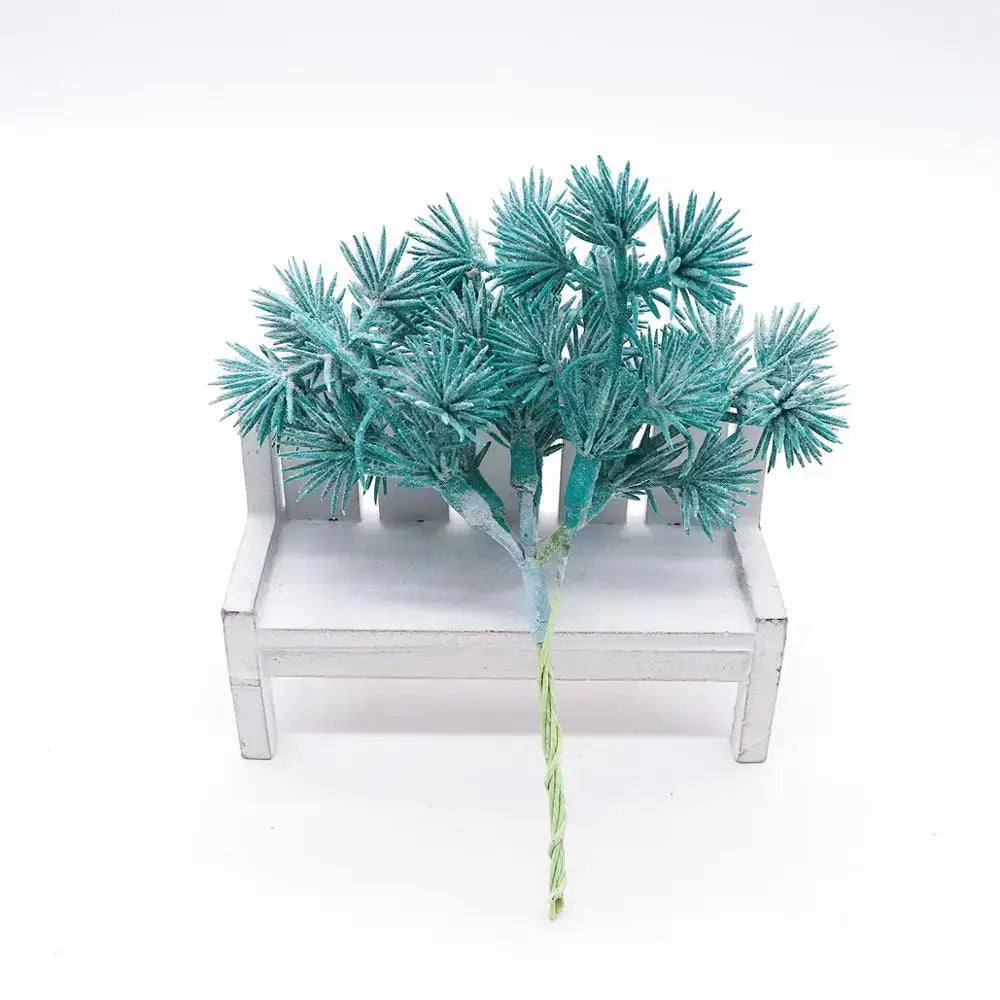 A teal frosted artificial pine branch with spiky needles on a white wooden bench for decorbites blue flower cherry decor