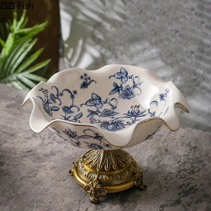 A white ceramic fruit bowl with blue flower pattern and gold trim on an ornate decorbites flower pattern footed base