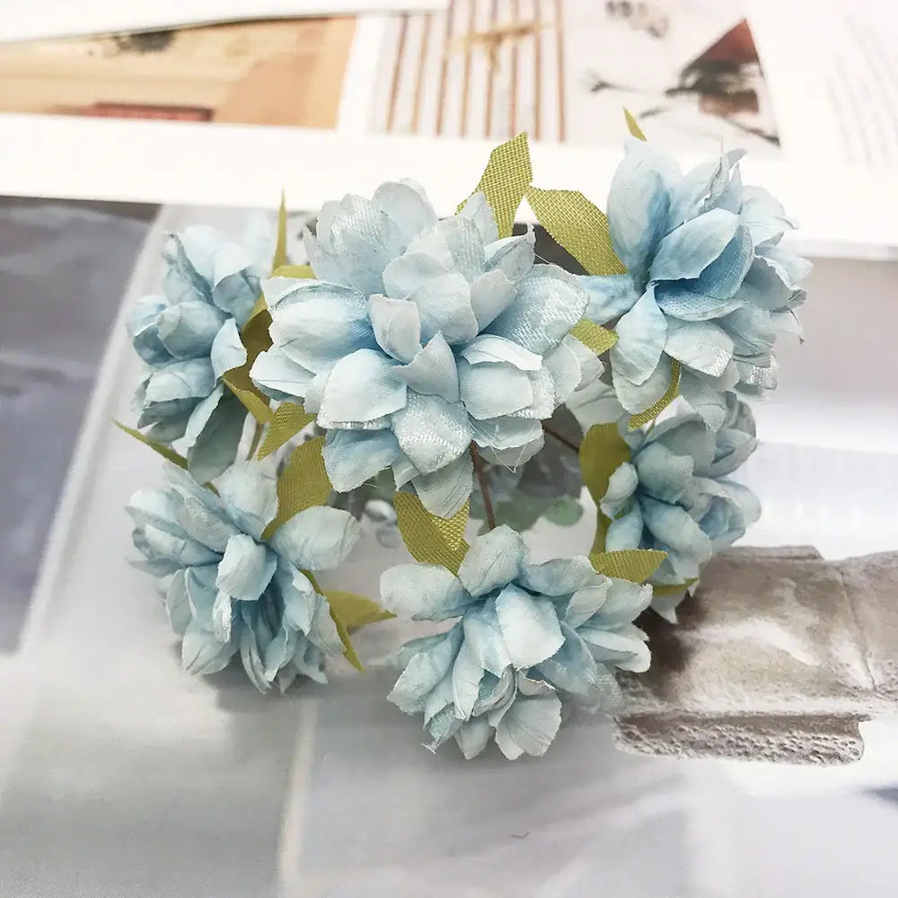 A delicate cluster of light blue fabric blue flower stamen with green leaf accents in a stamen berries bundle for decor