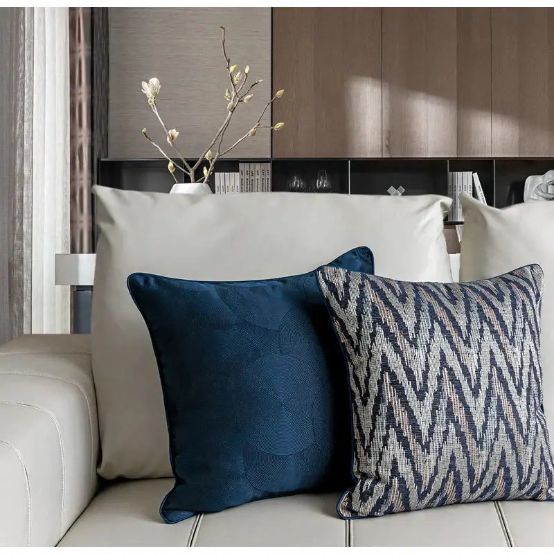 Two decorative throw pillows with blue geometry jacquard pillow cover and textured ikat pattern on a white sofa