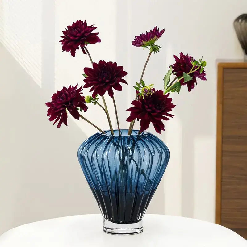 A translucent blue glass hot air balloon vase with vertical ridges and maroon dahlias for living room decor