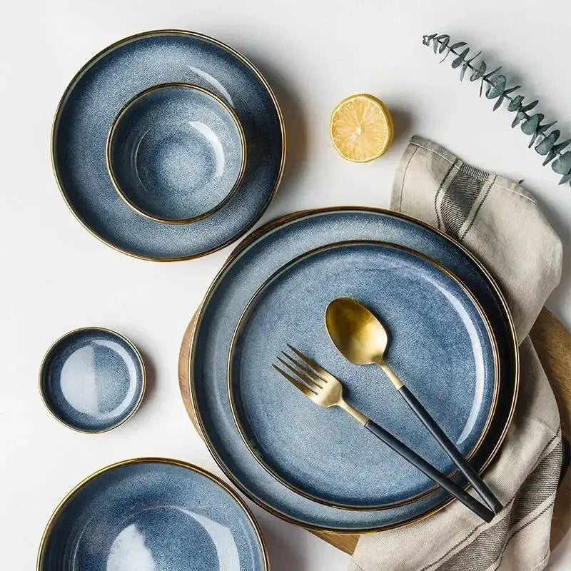 Blue gradient ceramic plate set with gold rims paired with black-handled cutlery for elegant dining room use