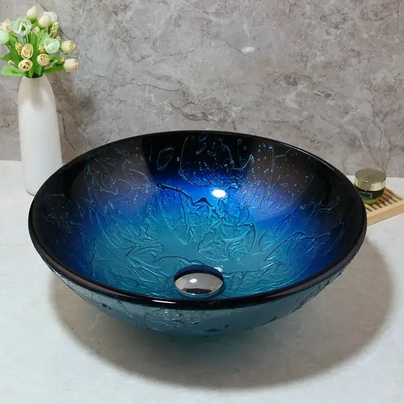 A vibrant blue gradient tempered glass basin sink set with swirling texture and sleek metallic drain for bathroom use