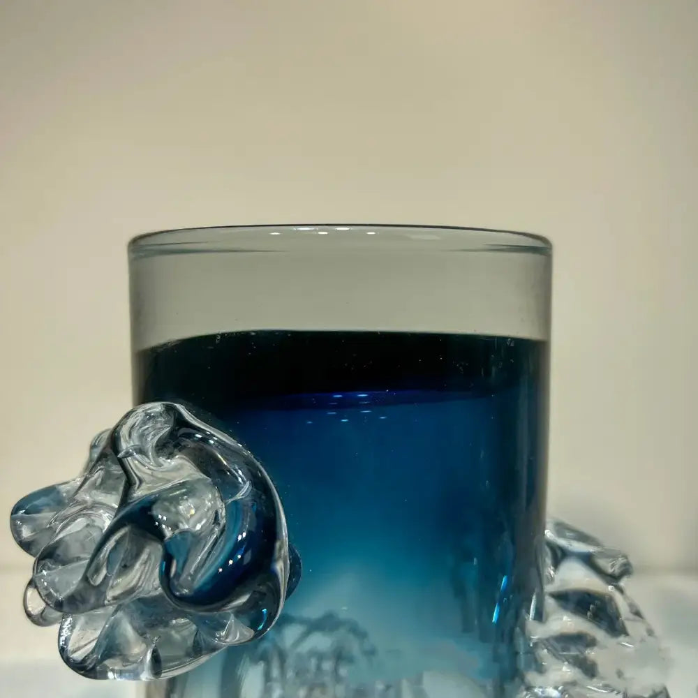 Clear glass mug with a sculpted transparent handle resembling an abstract hand and blue gradient wavy vase decor