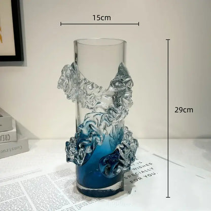 A tall transparent glass vase with a blue gradient wavy base and sculpted wave embellishments for living room decor
