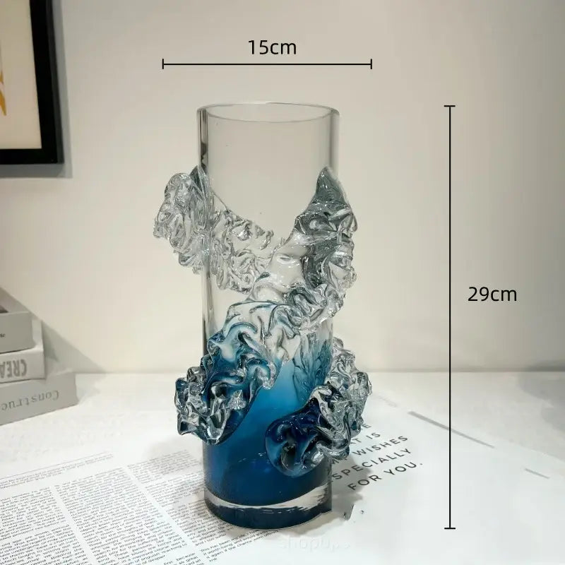 A tall transparent glass vase with a blue gradient wavy base and sculpted wave embellishments for living room decor