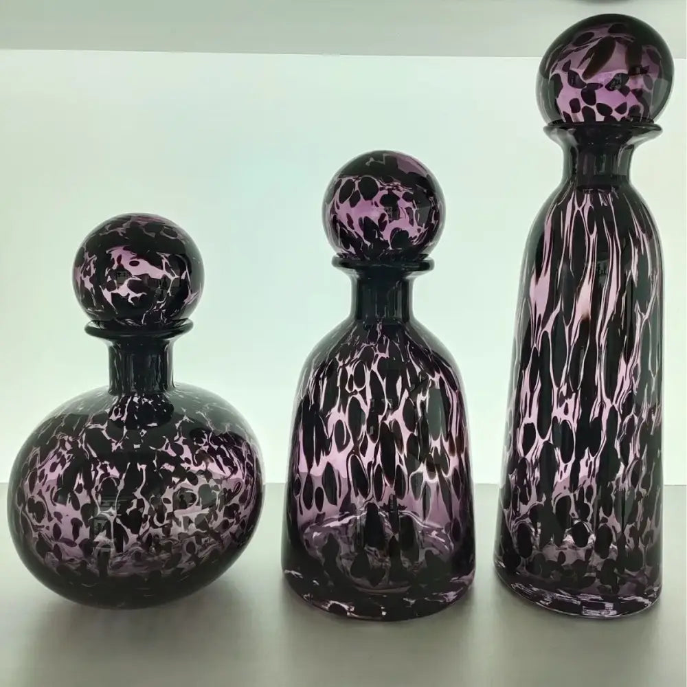 Three elegant glass decanters with purple and black swirling marble pattern and leopard print glass stoppers for decorbites decor