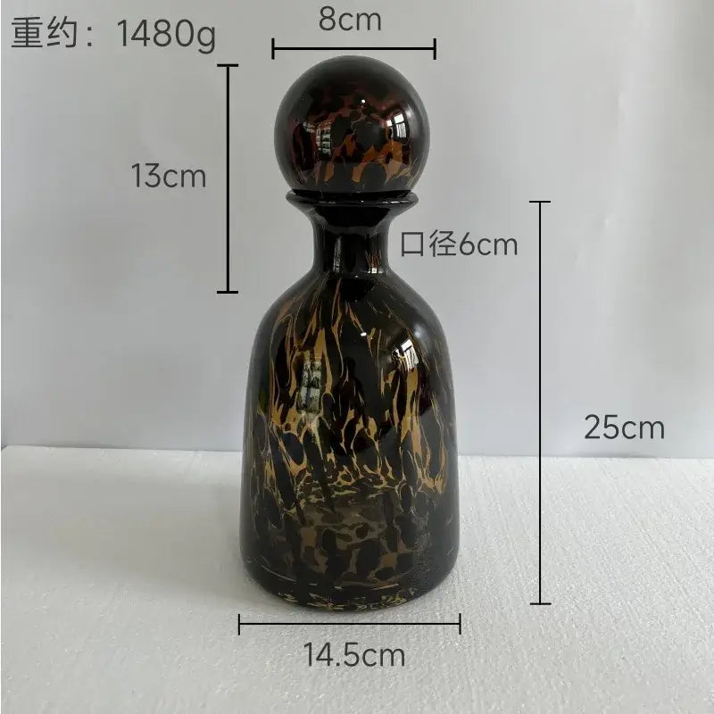 A glossy black glass decanter with swirling gold and brown marbled patterns and a spherical stopper decorbites leopard print decor