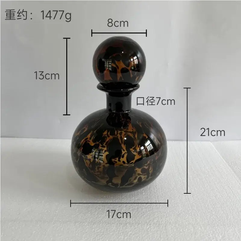 A glossy black glass perfume bottle with swirling amber and gold marbled pattern and spherical stopper decorbites leopard print
