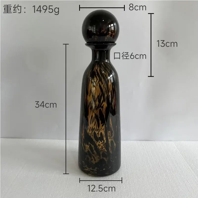 A tall glossy black glass decanter with swirling amber and gold marbled patterns and spherical cap decorbites leopard print