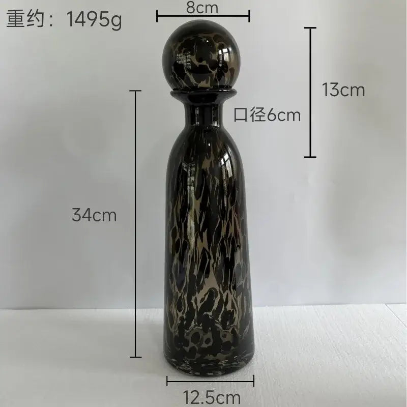A tall glossy black glass decanter with swirling gold and dark leopard print glass vase design and a spherical stopper decorbites leopard print