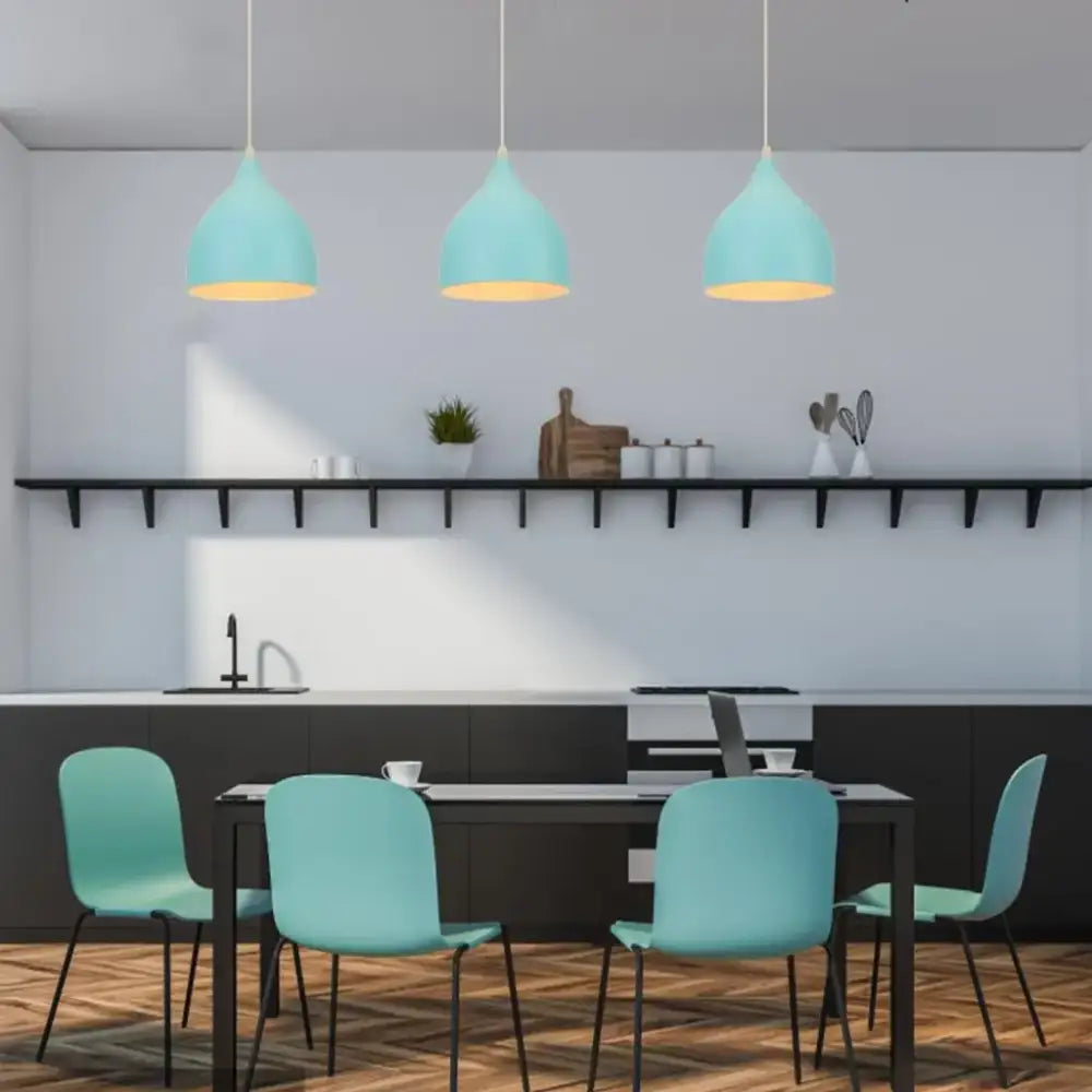 Three teal blue nordic pendant lights with matte metal and brass fixtures hang above a dining table for decorbites
