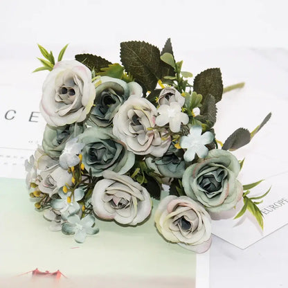 A delicate bouquet of silk fake flowers featuring blue peony and tea rose in soft sage green pale pink and cream hues