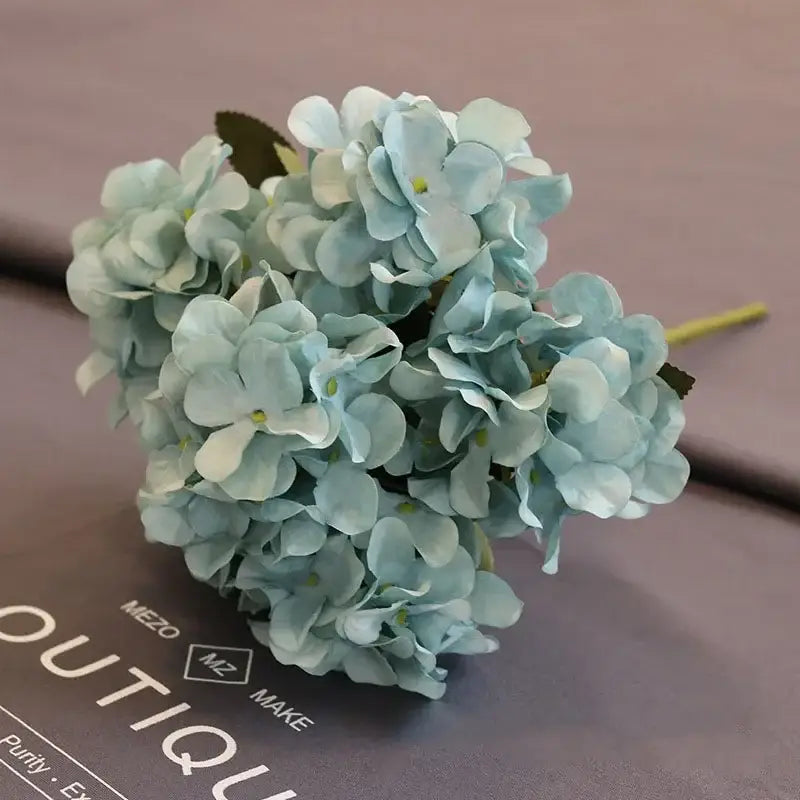 A delicate cluster of light blue silk fake flowers with layered petals and green centers for home garden decor