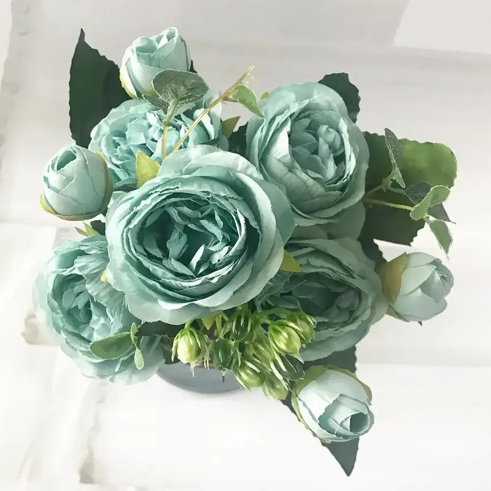 A bouquet of silk fake flowers featuring mint green tea rose and blue peony petals with dark green leaves for home decor