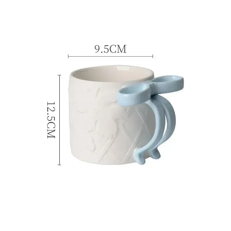 A white ceramic bowknot mug with light blue sculpted handle and embossed pattern from decorbites saucer set