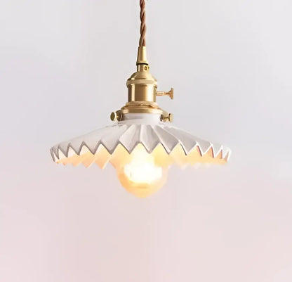 A vintage-style decorbites pendant light with brass fixture and white scalloped glass shade hanging by twisted cord
