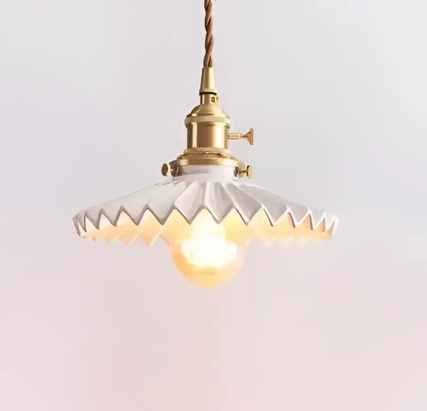 A vintage-style decorbites pendant light with brass fixture and white scalloped glass shade hanging by twisted cord