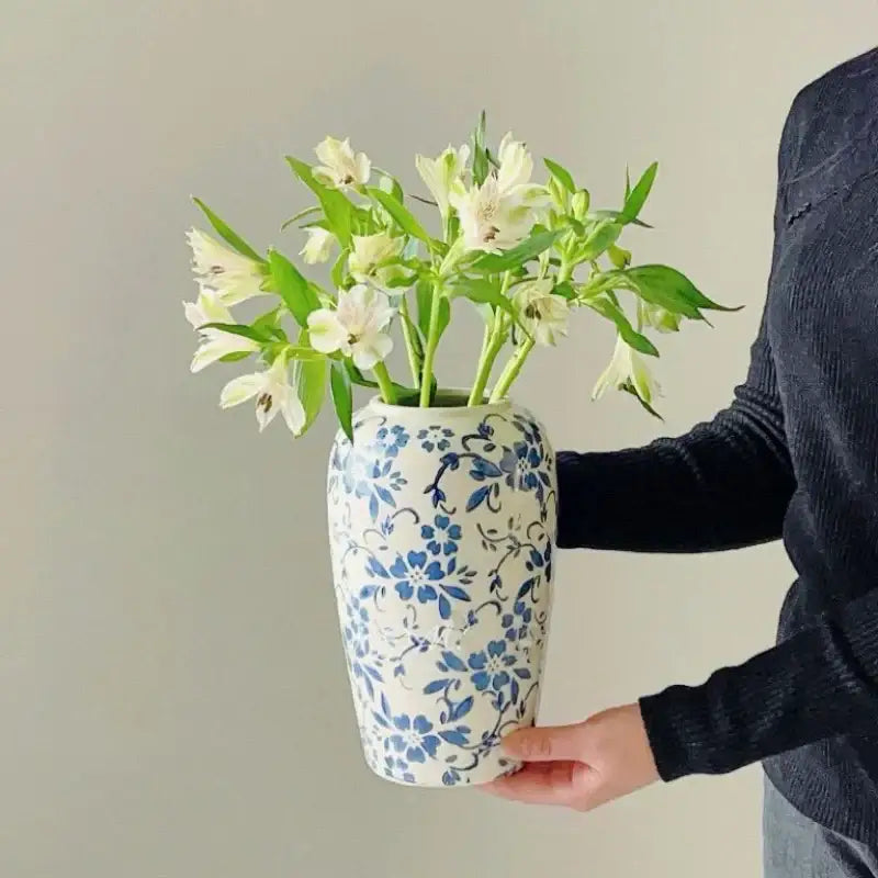 A white ceramic vase with blue floral patterns holds white flowers for decorbites blue living room decor