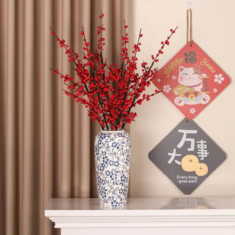A tall white ceramic vase with blue floral decorbites blue patterns holding red berry branches for living room decor