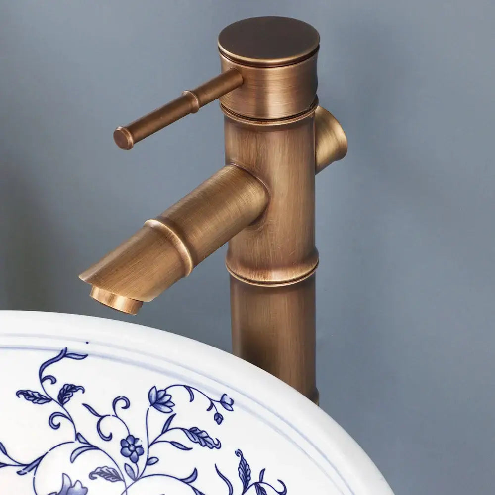 Antique brass bamboo-style faucet with brushed finish and cylindrical spout for blue and white porcelain basin set with pop drain
