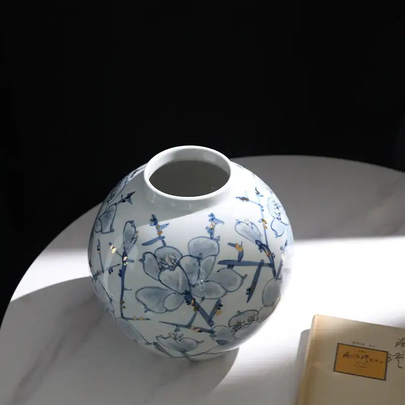 A round white porcelain ceramic vase with blue floral patterns and gold accents for living room decorbites decor