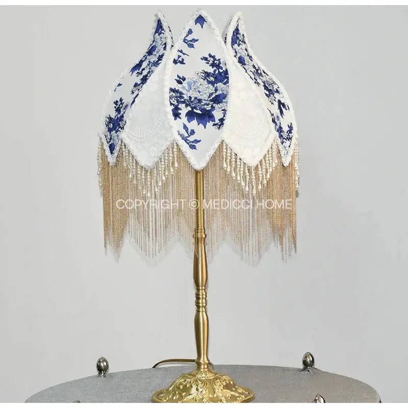 Elegant table lamp with a white porcelain floral lampshade featuring blue patterns and pearl tassel on brass base