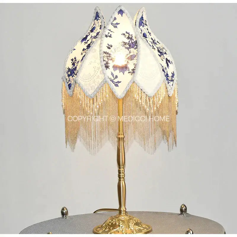 Decorative table lamp with gold metal base and white porcelain floral lampshade featuring pearl tassel trim