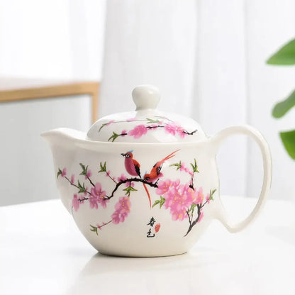 White porcelain tea pot set featuring delicate pink cherry blossoms and vibrant birds with elegant hand-painted details