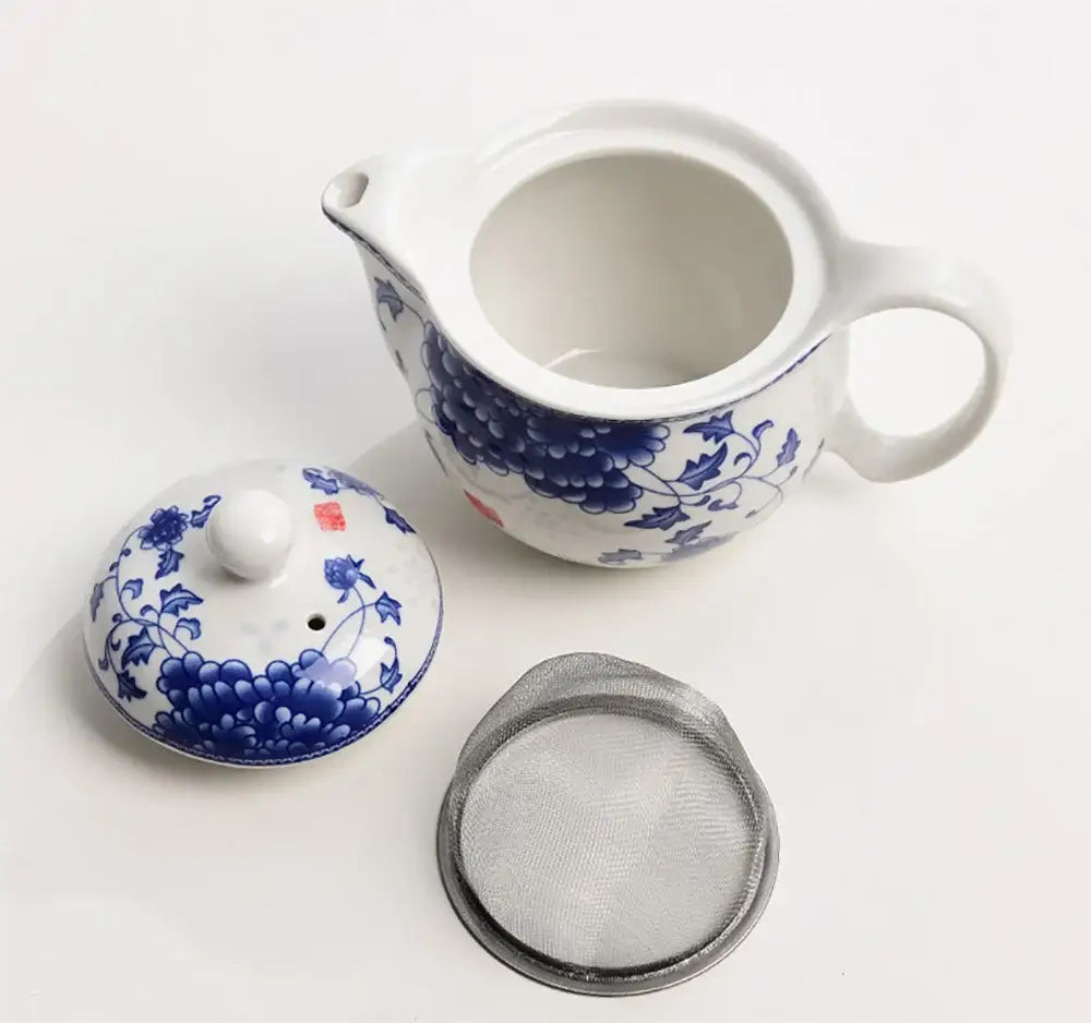 White porcelain tea pot set with blue floral patterns and matching lid accompanied by stainless steel strainer