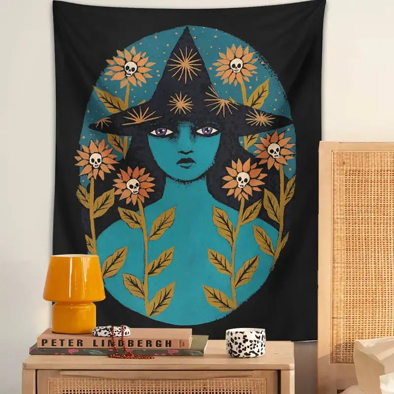 A black blue witches botanical tapestry featuring a teal skinned witch with a pointed hat and orange skull flowers wall art