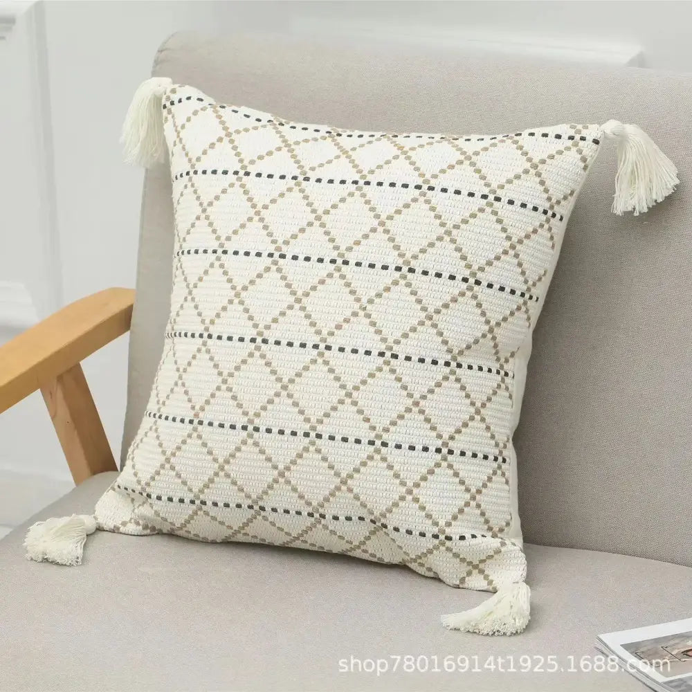 Cream-colored woven cushion cover with black and beige geometric diamond pattern and bohemian tufted tassel accents
