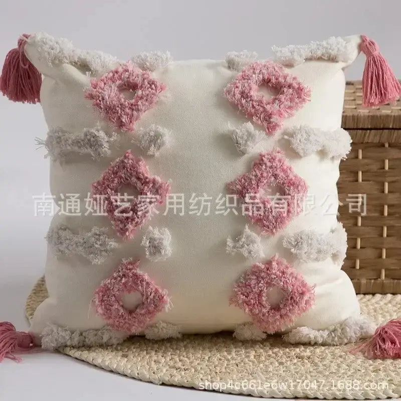 Cream-colored cushion cover with pink and gray bohemian tufted tassel diamond patterns and fringed corners decorbites