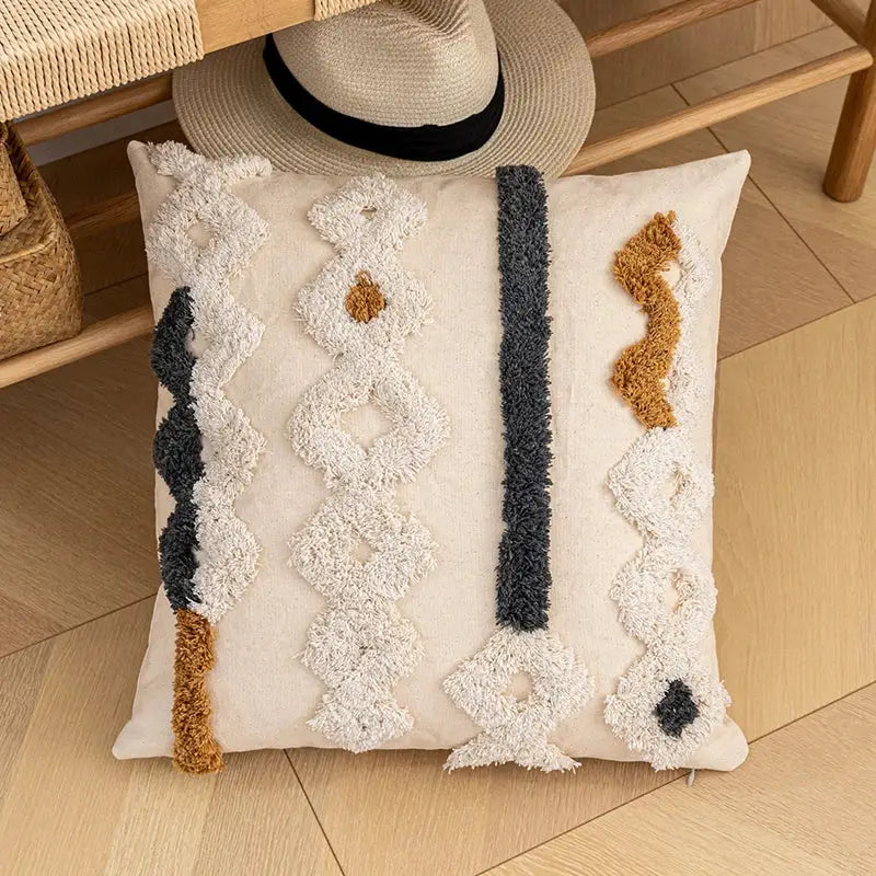 Cream-colored bohemian beige cushion cover with textured tufted geometric patterns in black and caramel brown yarn