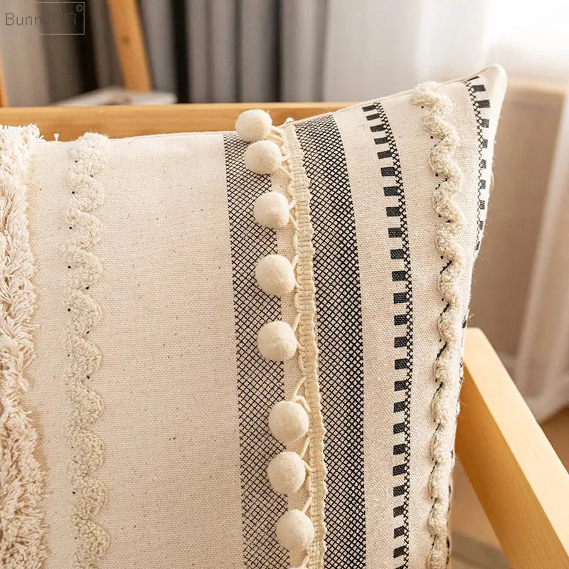 Cream-colored bohemian beige striped cushion cover with black and white pom-poms for home decor by decorbites