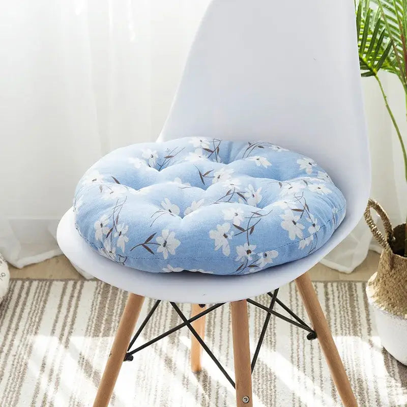 Light blue floral-patterned round meditation cushion pouf with tufted design on white chair for living room use