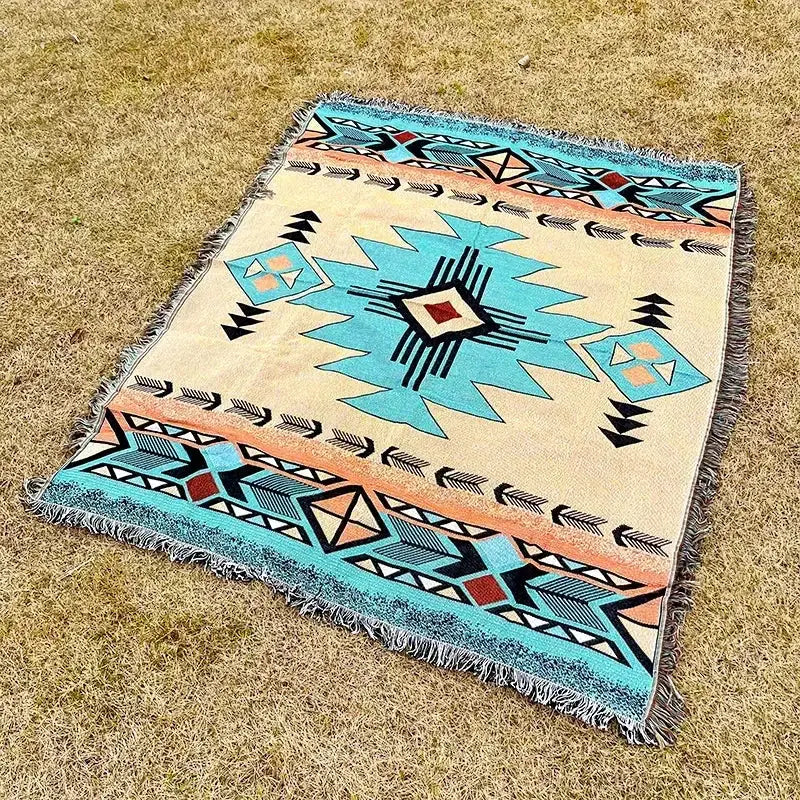 A cream-colored woven throw blanket with turquoise and black geometric tribal pattern and fringed edges by decorbites bohemian classic design
