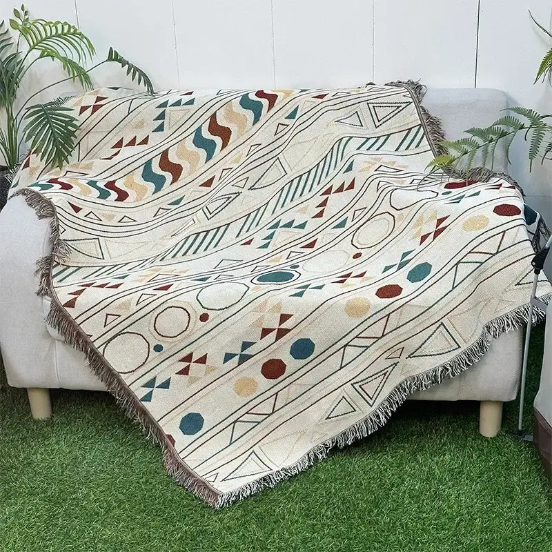 A cream-colored woven throw blanket with a bohemian classic design featuring earthy geometric patterns and fringed edges