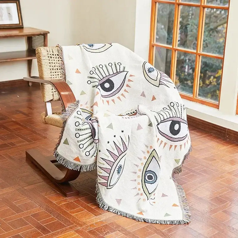 A cream-colored woven bohemian classic design thread throw blanket with purple and blue eye patterns for bedroom decorbites